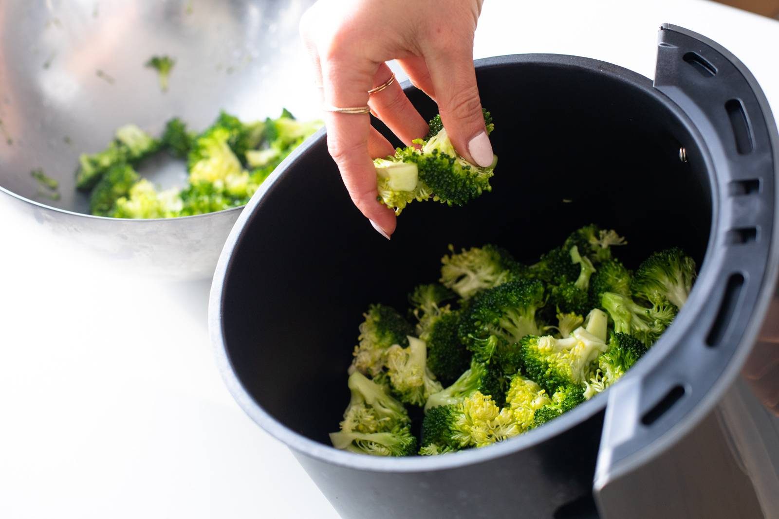 Adding broccoli to an air fryer.