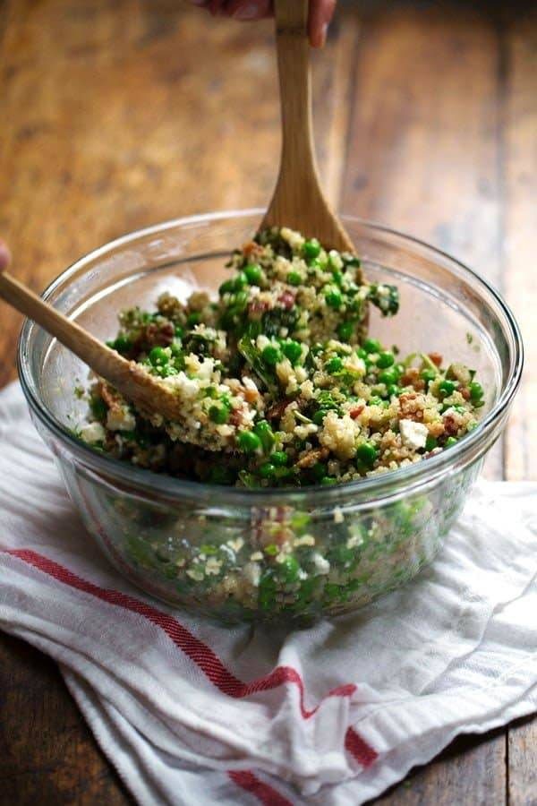 Quinoa Salad in a clear mixing bowl with two wooden spoons.