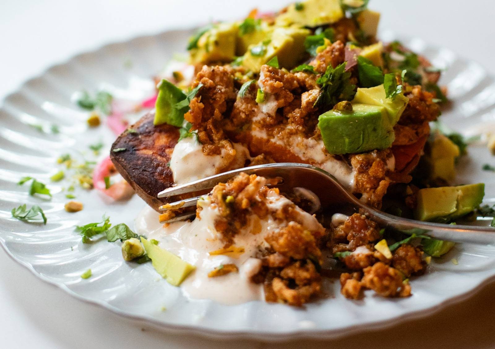 Roasted sweet potatoes with ground chicken, avocado, sauce, and herbs.