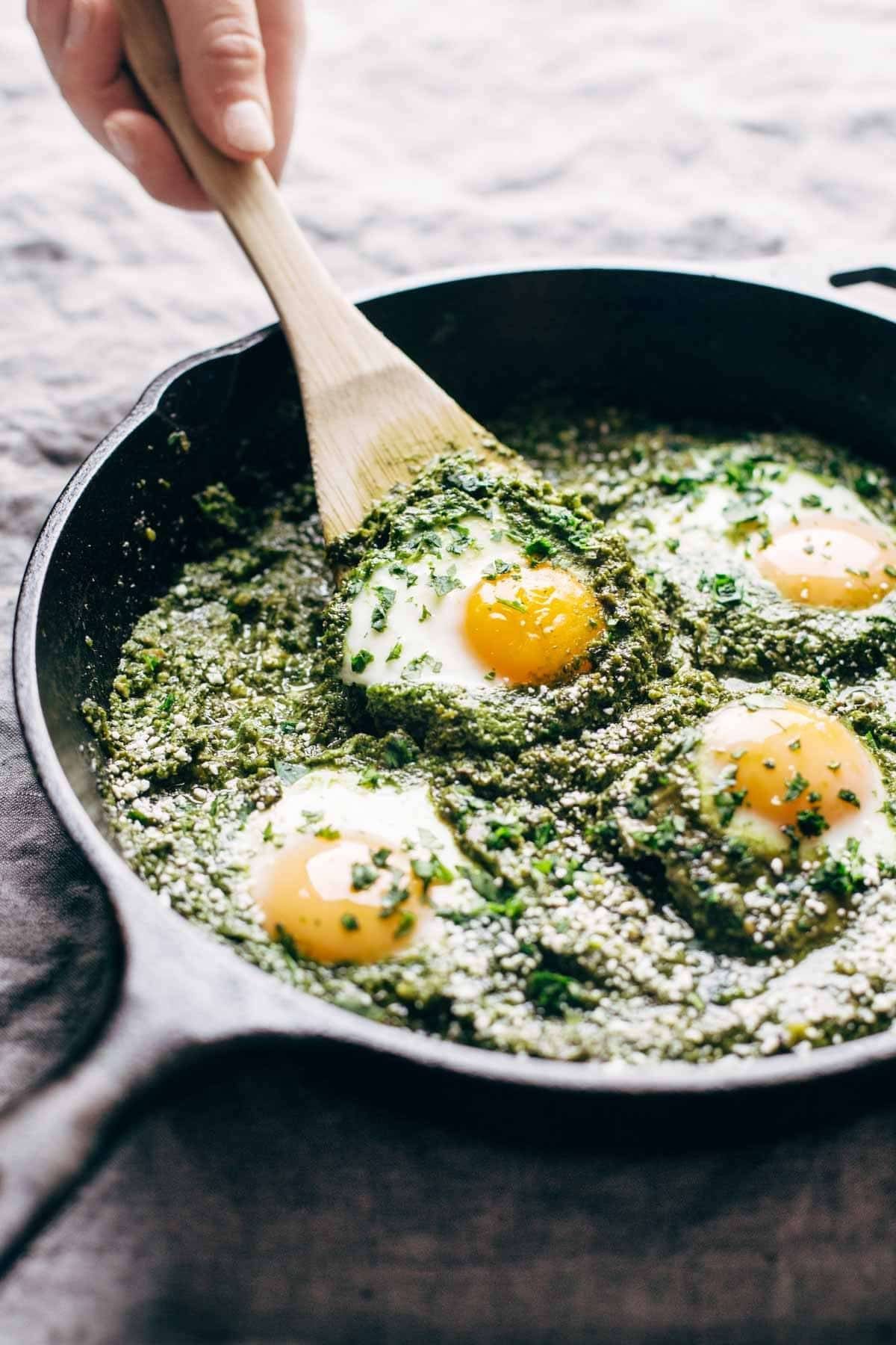 green shakshuka in a pan with a wooden spoon