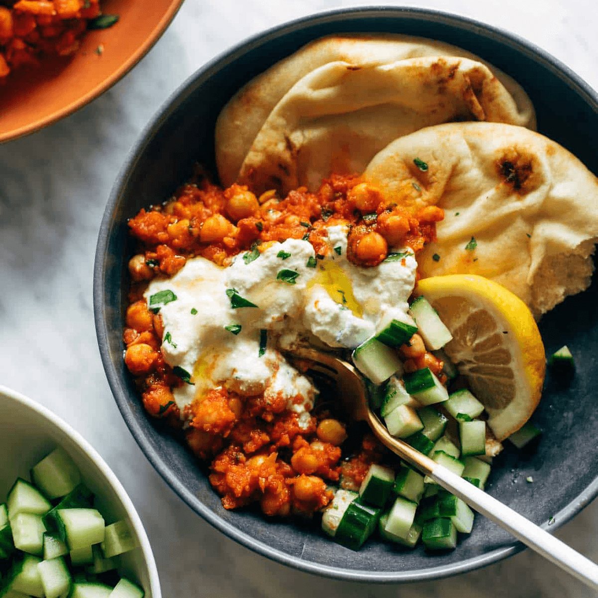 Harissa chickpeas in a bowl with cucumber, naan, and whipped feta.
