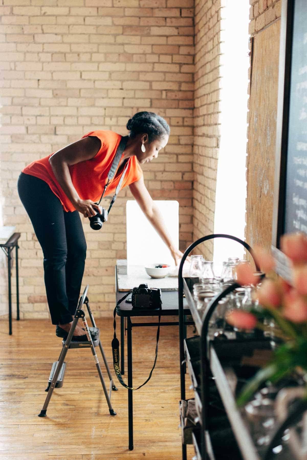 Woman standing on a step ladder arranging food for a photo.