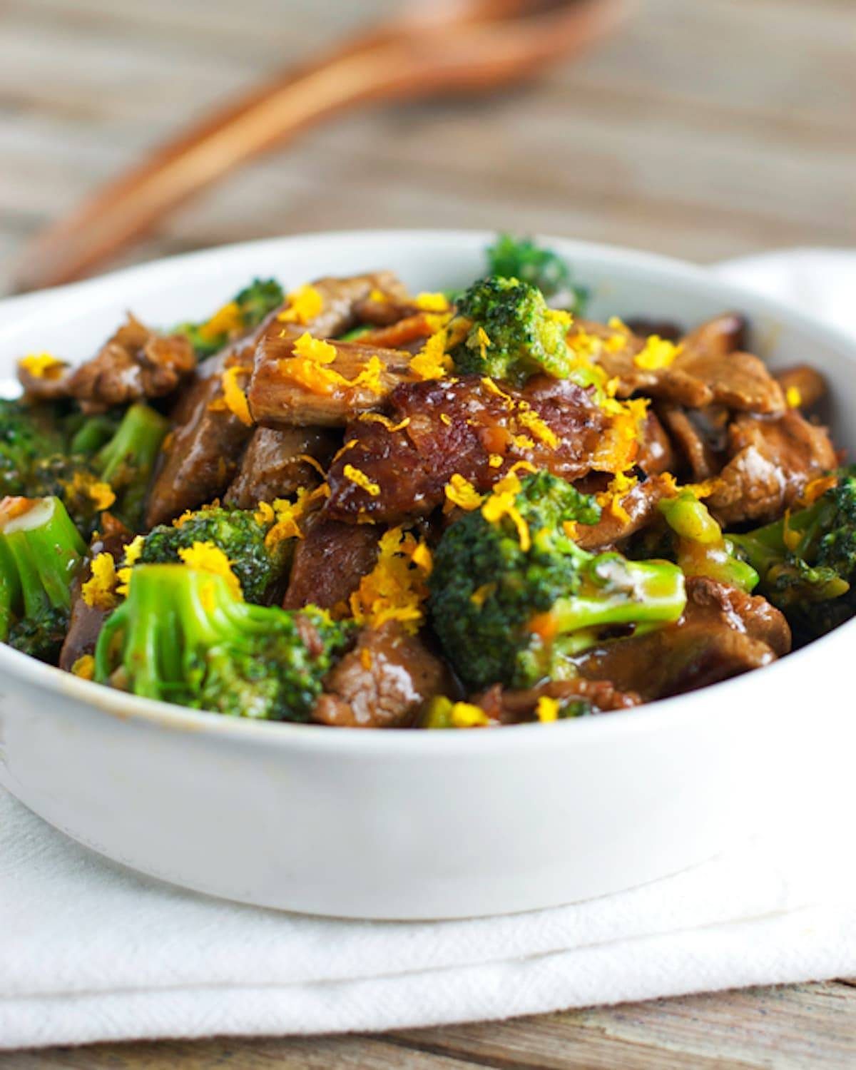 Light orange beef and broccoli in a bowl with orange zest.