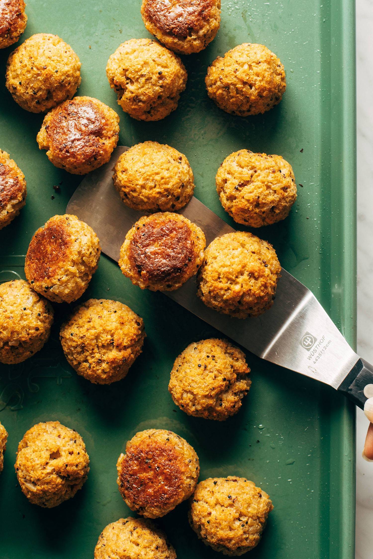 Cauliflower vegetarian meatballs on a sheet pan with a spatula.